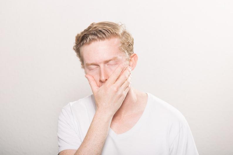 A man in a white shirt holding his face in his hand